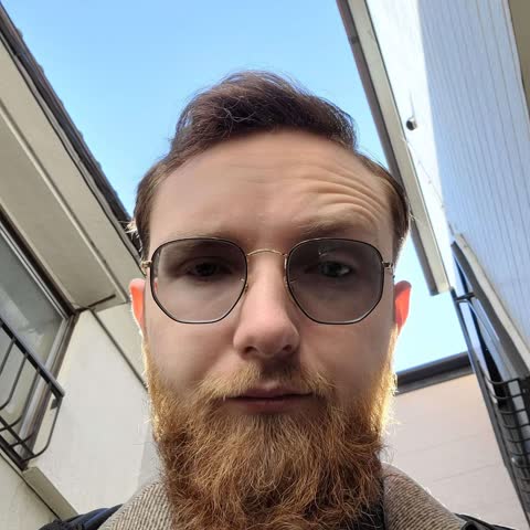 Kane outdoors, wearing wire-frame glasses